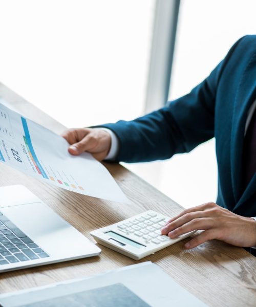 cropped view of man holding paper with lettering and counting on calculator